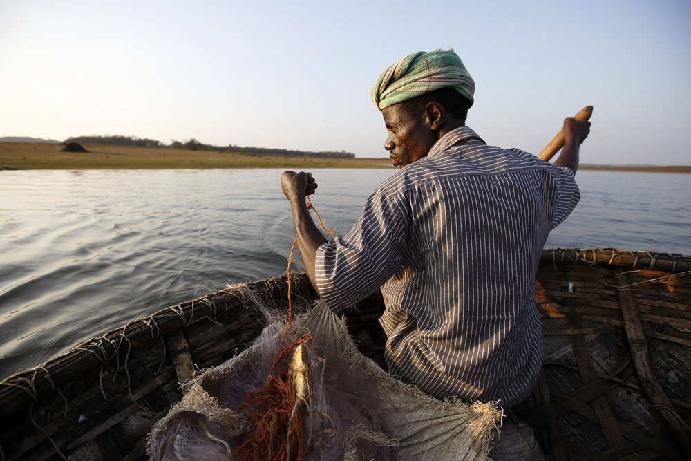 A Sidi man fishes on a dam reservoir in a traditional conicle boat. Uttara Kanada, India